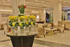 A spacious lobby with a round table, several sofas, and a large vase of yellow flowers. - Carawan Al Fahad Hotel (Riyadh)