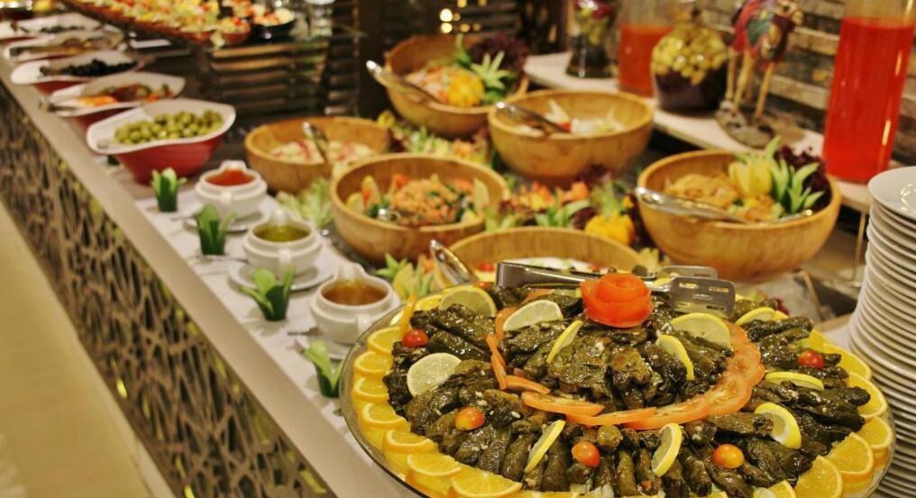 A buffet with various dishes, including a central platter of stuffed grape leaves garnished with lemon slices and tomatoes.