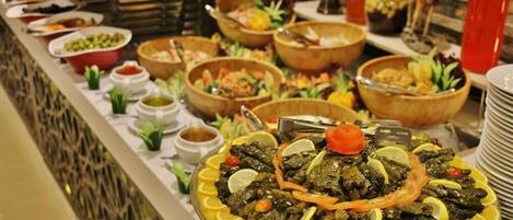 A buffet with various dishes, including a central platter of stuffed grape leaves garnished with lemon slices and tomatoes.
