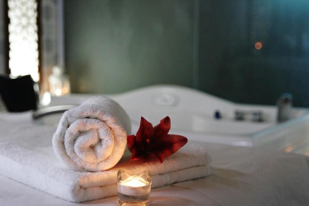 A neatly rolled white towel, a red flower, and a lit candle on a marble surface.