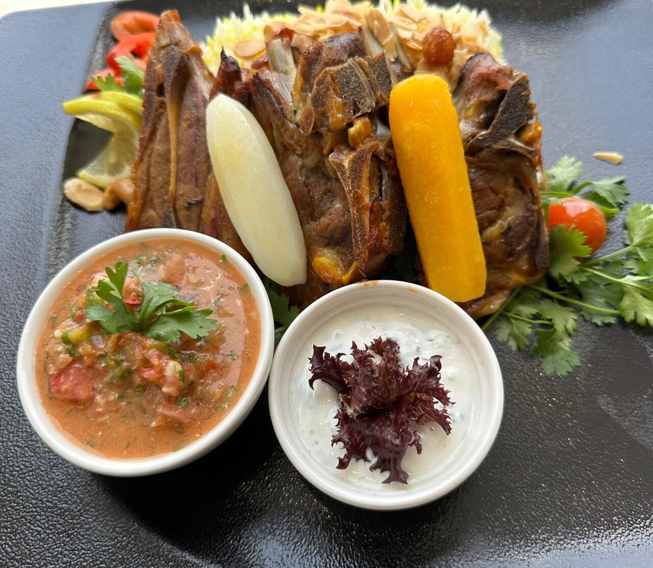 A plate of food with a variety of meats, vegetables, and two small bowls of sauce.
