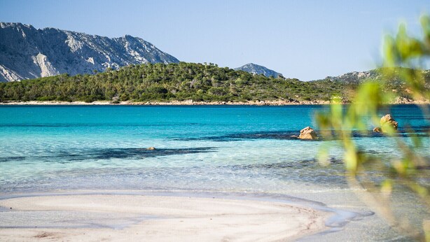 Una playa con agua turquesa cristalina, una orilla de arena y una montaña al fondo.