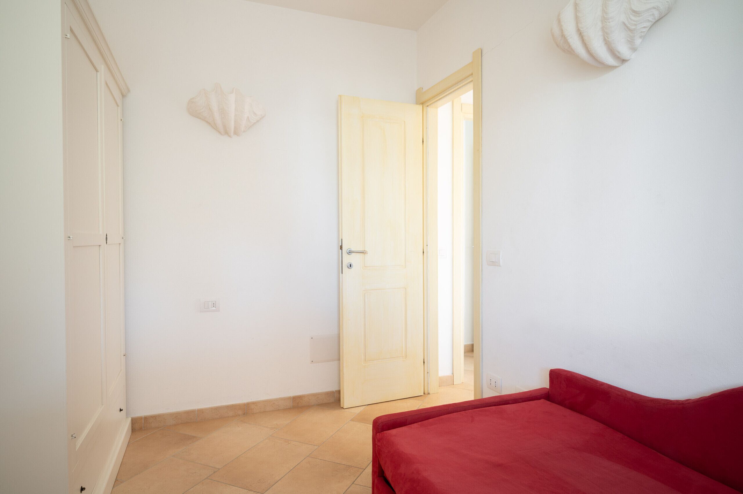 A room with a red sofa, a wooden door, and a white wall with a shell decoration.