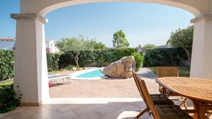 Un patio techado con piscina, una gran roca, una mesa de madera y sillas.