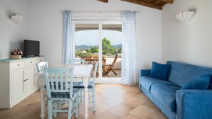 Un área de comedor con una mesa y sillas, un sofá azul y un televisor sobre un mueble.