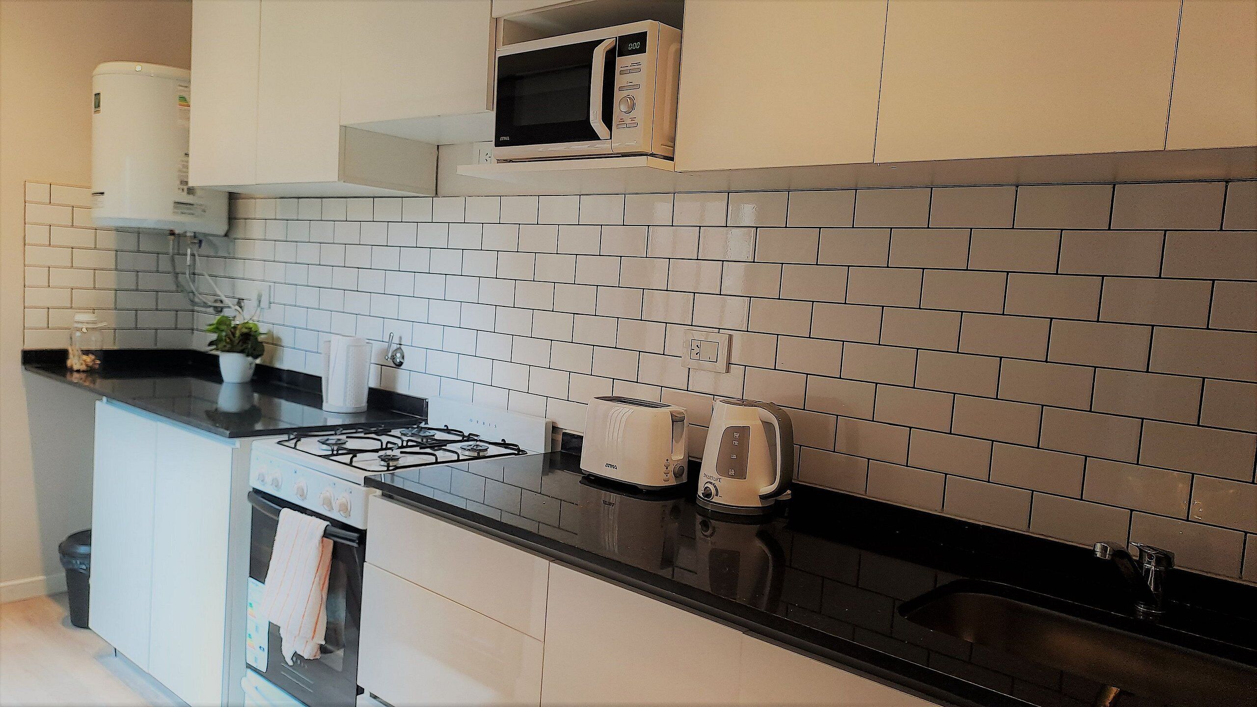 Eine Küche mit weißen Schränken, einer schwarzen Arbeitsplatte, einer Mikrowelle, einem Toaster und einem Wasserkocher.