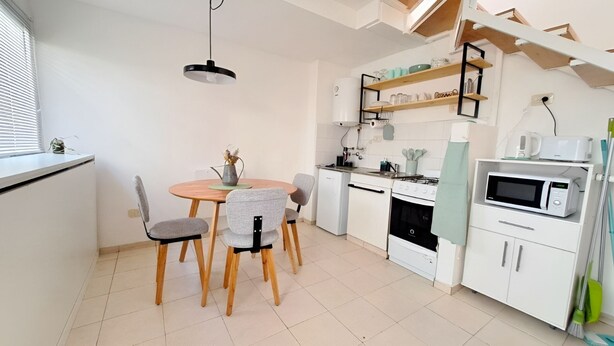 Een praktische keuken met een eettafel, stoelen, een kookplaat, magnetron en planken.