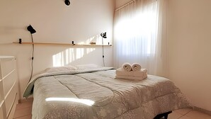 Een slaapkamer met een bed, nachtkastje, lamp en een raam met gordijnen.