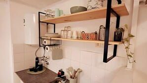 Een keuken met een spoelbak, aanrecht en planken met keukengerei en bestek.