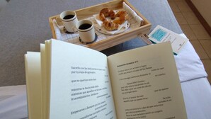 Ein Tablett mit Croissants und Kaffeetassen auf einem Bett mit einem offenen Buch.