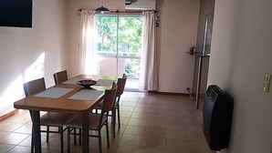 Ein Essbereich mit Tisch und Stühlen, ein Fenster mit Vorhängen und einem Heizkörper an der Wand.