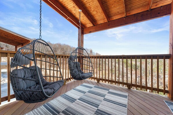 A wooden deck with two hanging chairs and a striped rug.