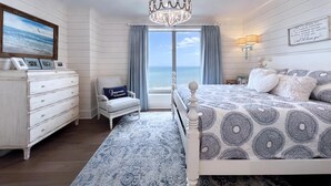 Ein Schlafzimmer mit einem großen Bett, einem Schminktisch, einem Sessel und Blick aufs Meer.