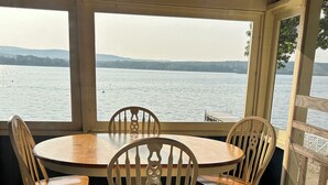 Un espacio de estar al aire libre cubierto, con una mesa redonda y cuatro sillas de madera, con vista a un cuerpo de agua.