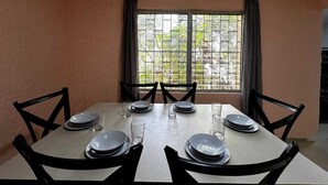Un coin repas avec une table dressée pour quatre personnes, six chaises et une fenêtre avec des rideaux.