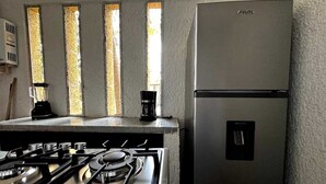 Une cuisine équipée d’une cuisinière à gaz, d’un réfrigérateur et d’une machine à café posée sur le plan de travail.