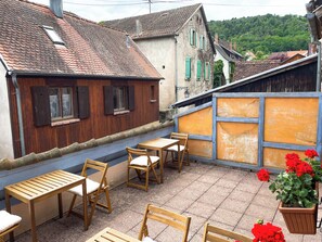 A courtyard with wooden furniture and a potted plant. - La Maison Bleue (Riquewihr)