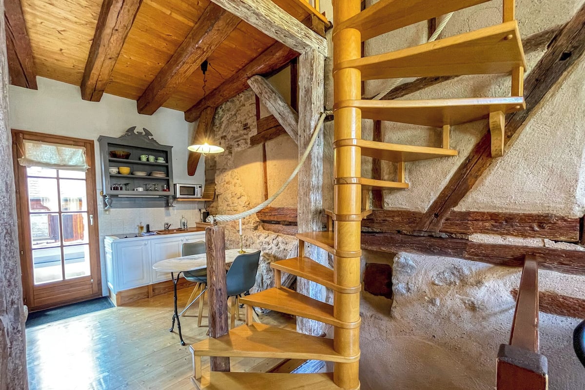 A spiral staircase in a rustic interior with exposed stone walls and wooden beams.