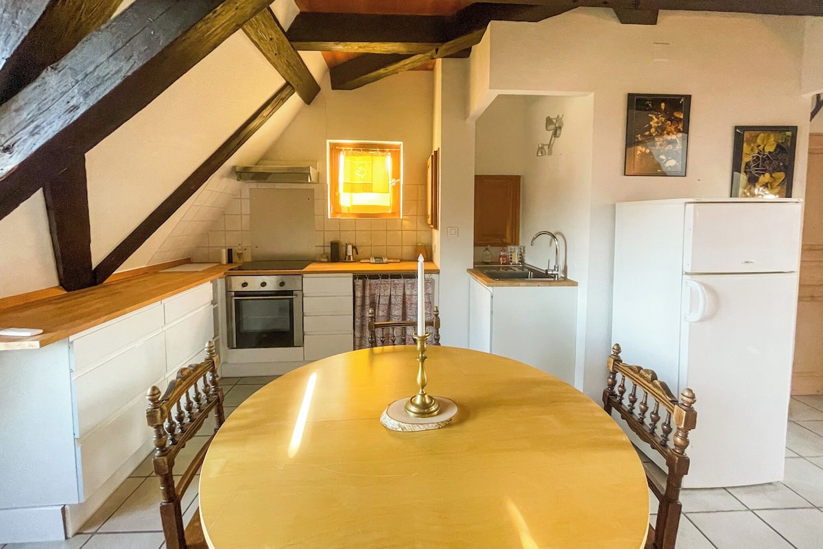 A kitchen with a dining table, oven, refrigerator, and a window with curtains.