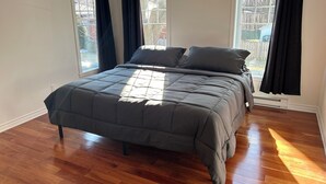 A bedroom with a bed, two windows, and a wooden floor. - Magnifique maison près de l'eau (Laval)