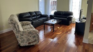 A living room with two black leather sofas, a floral armchair, and a wooden coffee table. - Magnifique maison près de l'eau (Laval)