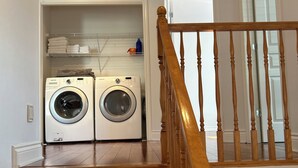 A laundry room with two front-loading washers and dryers, a wooden staircase with a railing, and a black leather couch in the adjacent living area. - Magnifique maison près de l'eau (Laval)