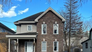 A two-story brick house with a garage, a covered porch, and a driveway. - Magnifique maison près de l'eau (Laval)