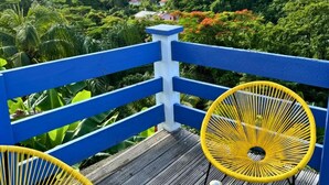 A wooden deck with blue railings, two yellow wicker chairs, and a small table with a glass vase and greenery. - T3 private pool - Paprika -Terrasses de la wallon (Les Trois Ilets)