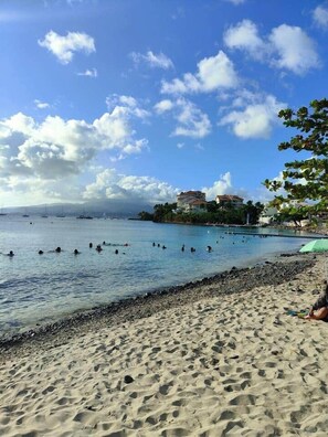 A beach with clear blue water, people swimming, and buildings in the background.