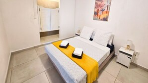 A bedroom with a bed, a nightstand, a painting, and a window with blinds. - T3 private pool - Paprika -Terrasses de la wallon (Les Trois Ilets)