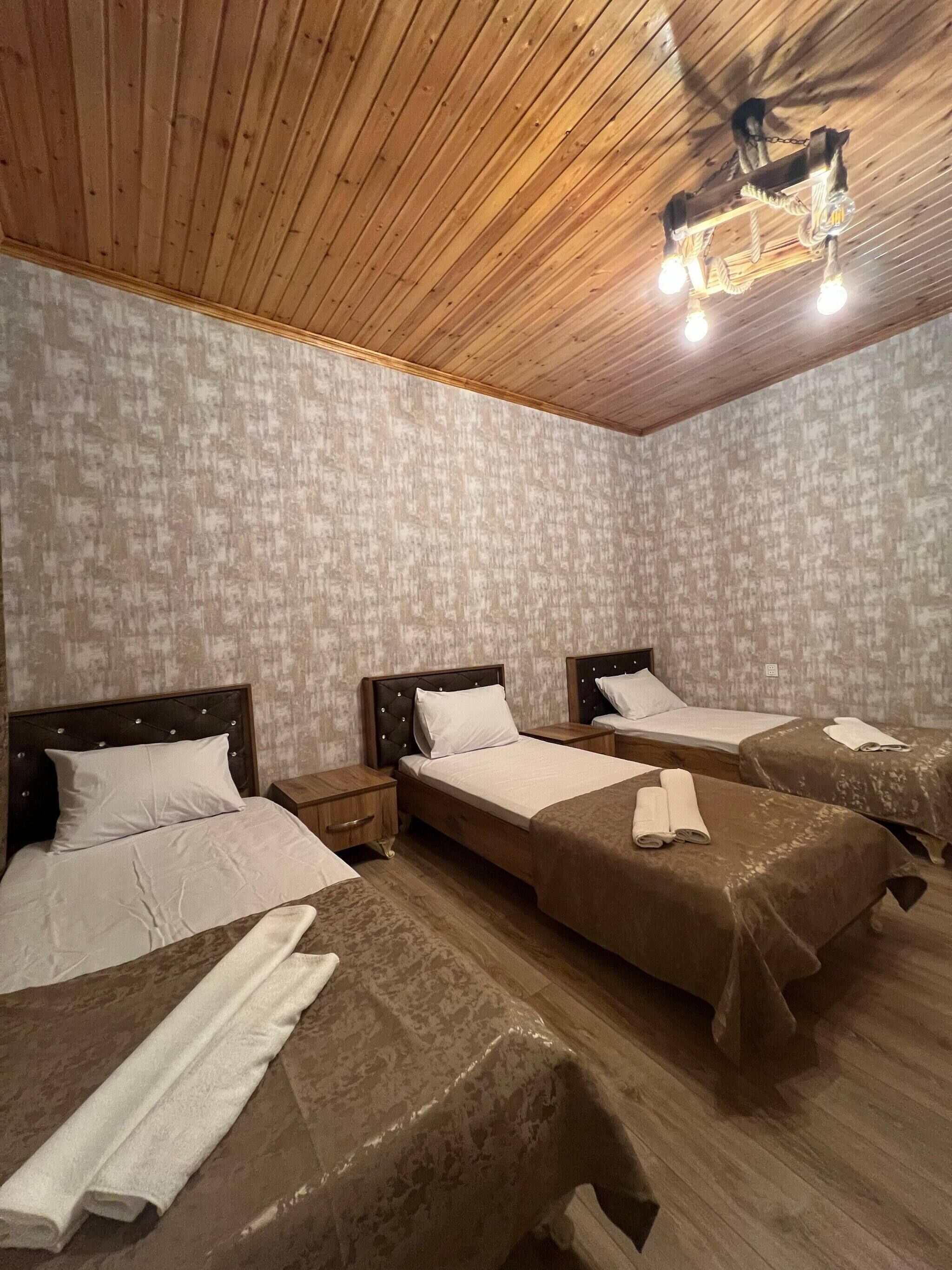 A room with three wooden beds, each with a headboard and a nightstand. The room has a wooden ceiling with a light fixture.