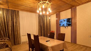 Un comedor con techo de madera, un candelabro, una mesa con sillas, un sofá y un televisor en la pared.