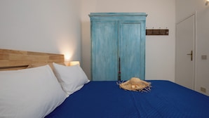 A bedroom with a wooden headboard, a blue bedspread, white pillows, and a blue wardrobe with a wooden coat rack above it. - Casa Girgolu by Wonderful Italy (San Teodoro)
