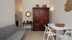A compact living space with a grey sofa, a wooden cabinet with baskets, a small table with chairs, and a wall-mounted mirror. - Casa Girgolu by Wonderful Italy (San Teodoro)