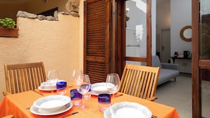 A dining table set with plates, glasses, and cutlery, with a wooden chair and a sofa in the background. - Casa Girgolu by Wonderful Italy (San Teodoro)