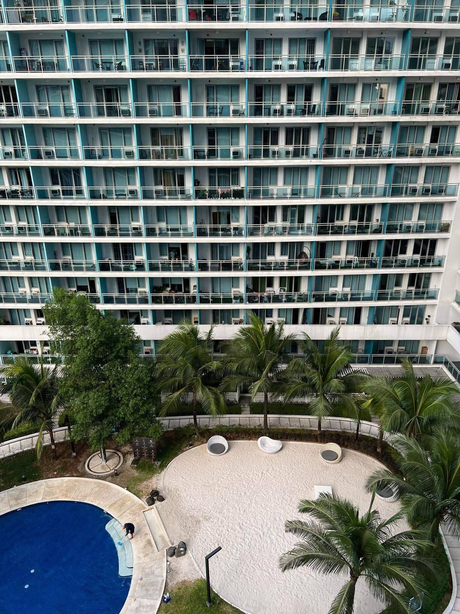 A multi-story hotel with balconies, a swimming pool, and palm trees.