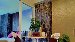 A modern room with a bed, two white chairs, a small table with a plant, and a large window. - Santorini Suites (Parañaque)