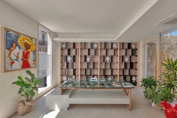 Un interior moderno con una mesa de vidrio, un cuadro abstracto grande y una pared de estantes con objetos decorativos.