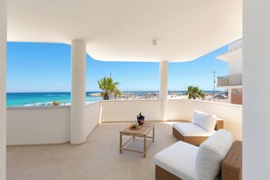Ein Balkon mit Meerblick, eine Rattan-Couch, ein kleiner Tisch mit einem Getränk und eine weiße Wand.