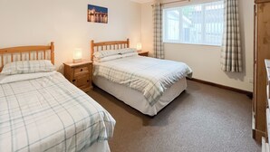 Une chambre avec deux lits, une fenêtre avec des rideaux, une table de chevet avec une lampe et un tableau accroché au mur.