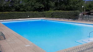 Une piscine rectangulaire à l’eau d’un bleu limpide, entourée d’une terrasse carrelée et d’une haie.