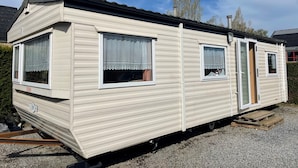 Une maison mobile dotée de deux fenêtres, d’une porte et d’un petit porche.