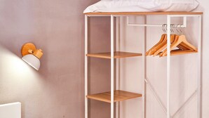 A closet with wooden shelves and a hanging rod, a light fixture on the wall, and a power outlet.