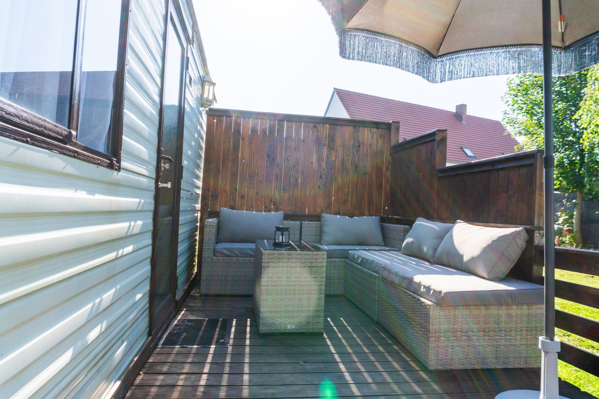 A covered patio area with a wicker sofa and a small table, surrounded by wooden fencing.