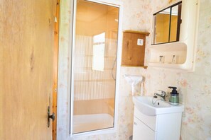 A bathroom with a wooden door, a shower, a sink with a mirror, and toiletries on the wall. - Base Camp for the Harz and City Tours Leipzig, Magdeburg, Dessau, Quedlinburg... (Gröbzig)