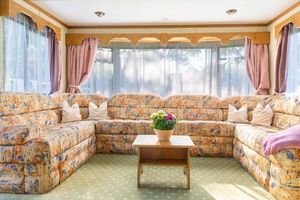 A cozy living room with a floral sofa, a wooden coffee table, and sheer curtains. - Base Camp for the Harz and City Tours Leipzig, Magdeburg, Dessau, Quedlinburg... (Gröbzig)