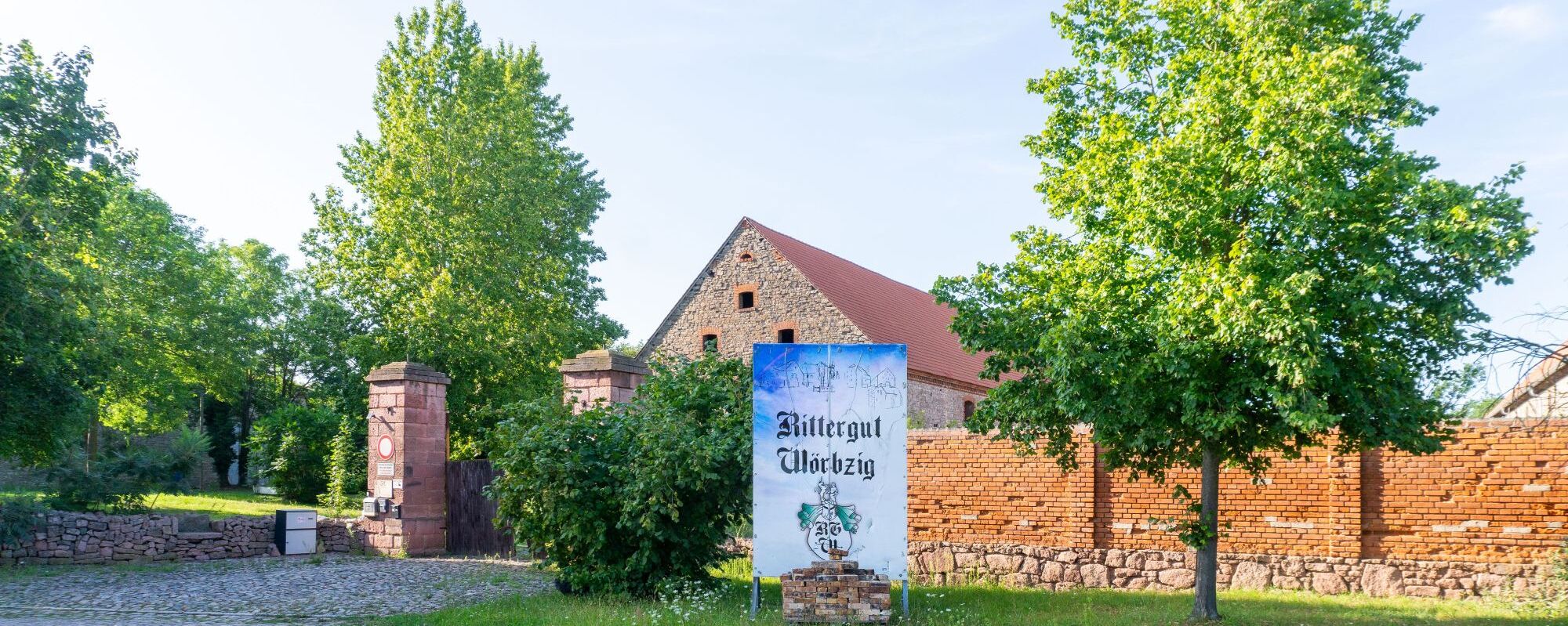 Un bâtiment historique à la façade en pierre et au toit rouge, entouré d’une végétation luxuriante.