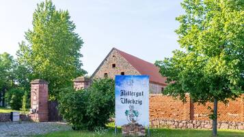 Un bâtiment historique à la façade en pierre et au toit rouge, entouré d’une végétation luxuriante.