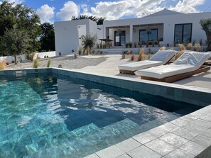 A modern pool area with clear water, lounge chairs, and a white building with large windows. - Casa Bartolomeu (Castro Marim)