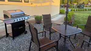An outdoor patio with a grill, chairs, and a table.
